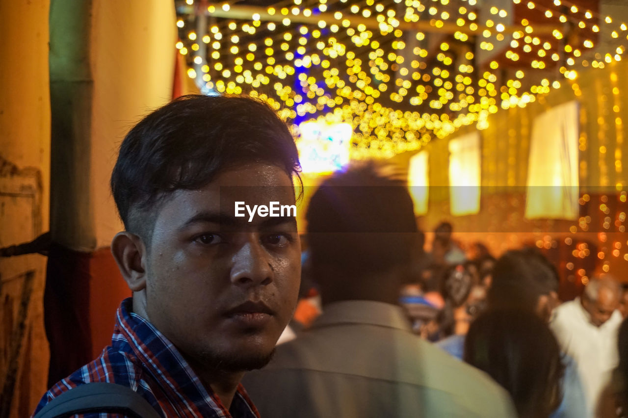 Close-up portrait of young man on illuminated street at night