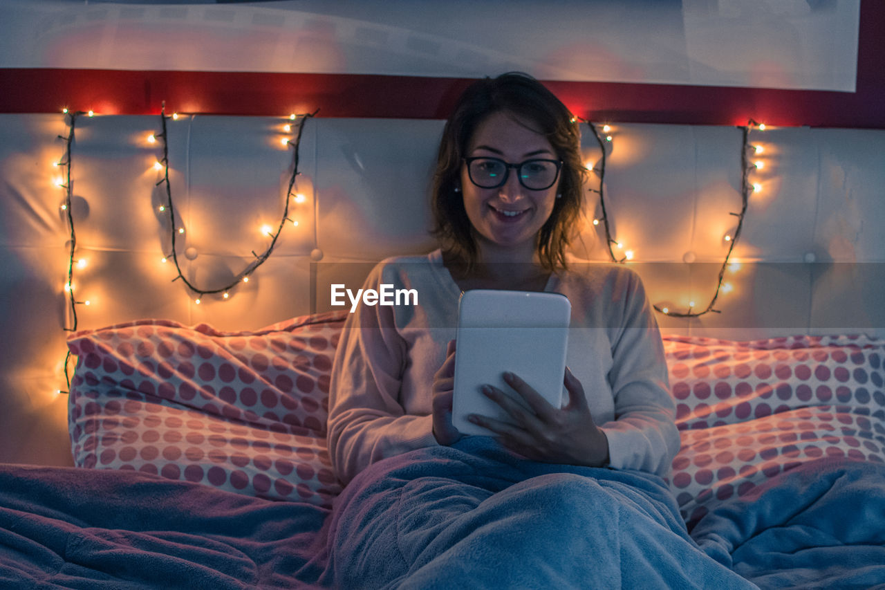 Young woman using digital tablet while sitting on bed at home