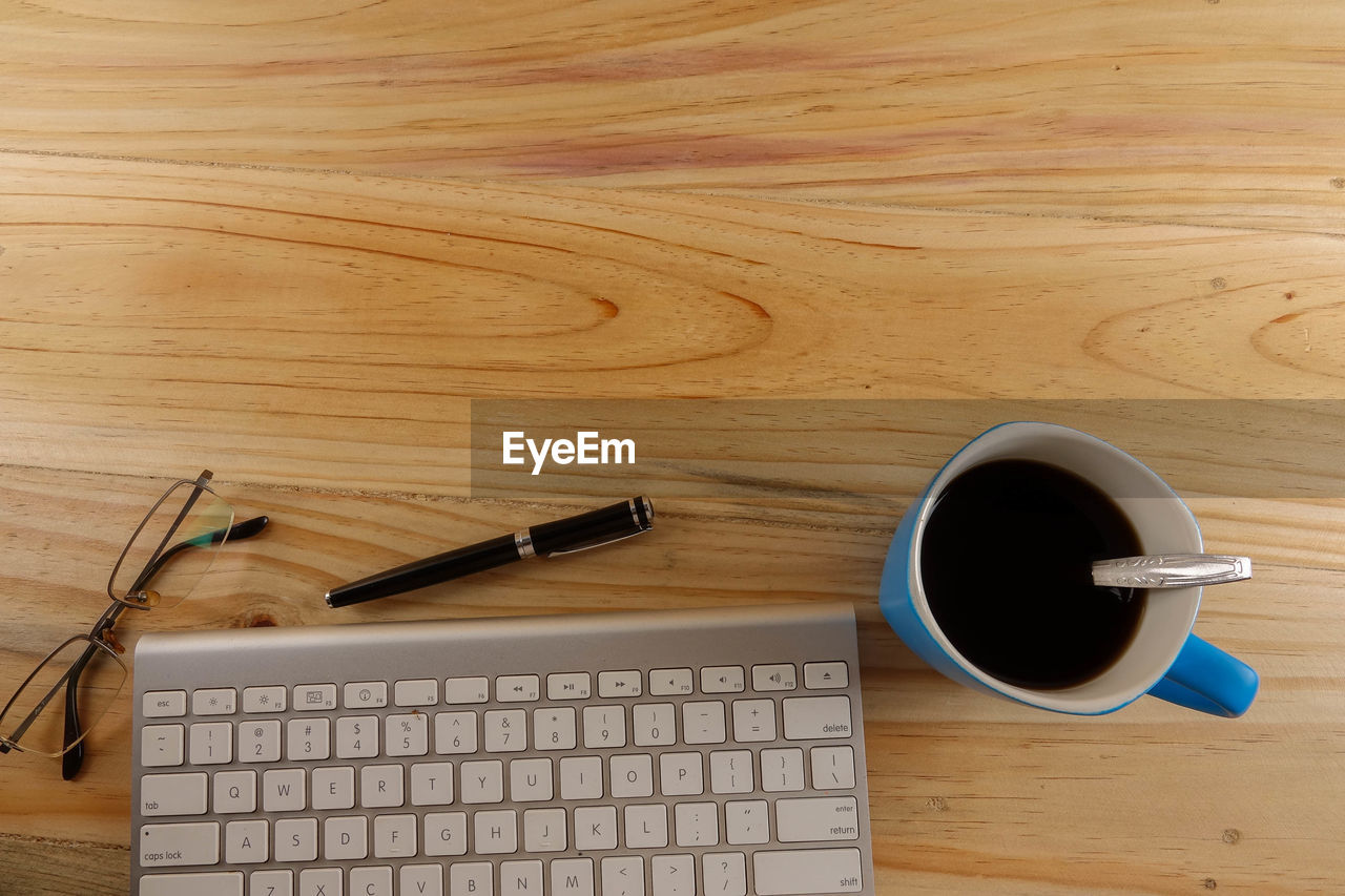 High angle view of coffee cup with laptop and eyeglasses by pen on wooden table