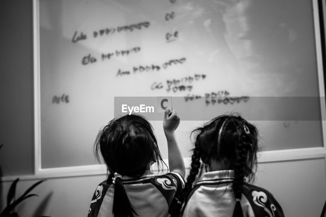 Rear view of girls standing in front of glass blackboard
