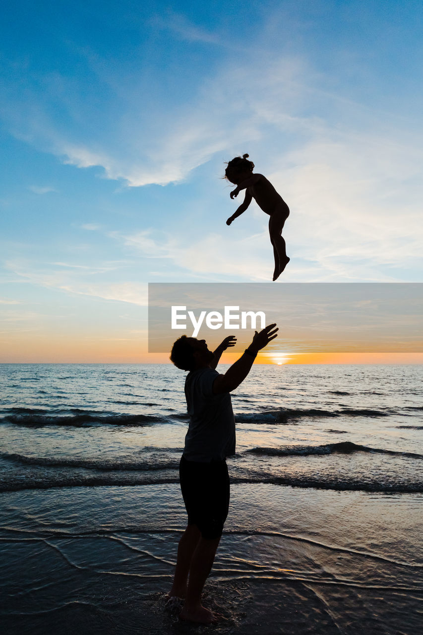 Dad throws his toddler daughter into the air at florida beach sunset