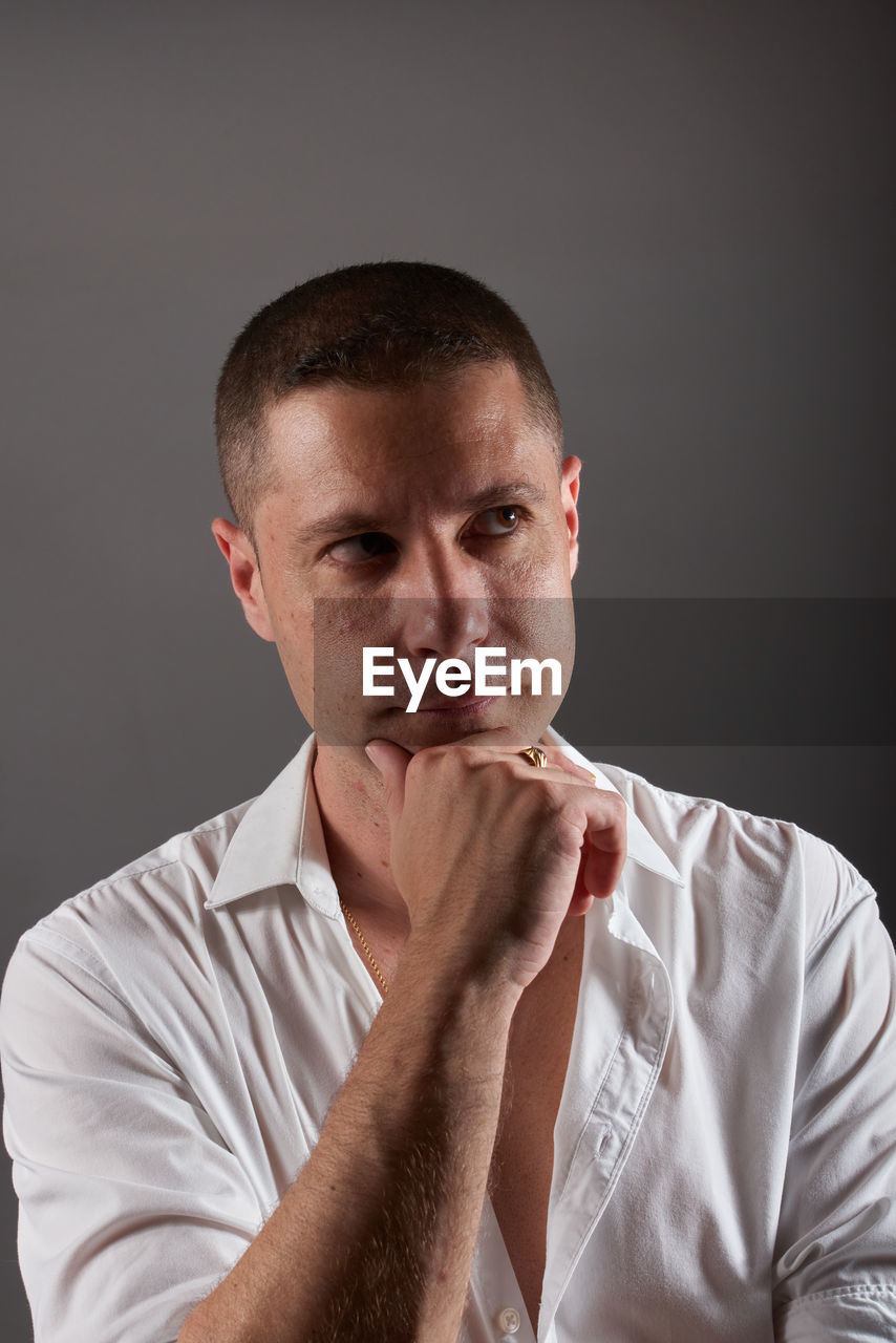 one person, studio shot, adult, portrait, men, indoors, person, gray background, gray, serious, buzz cut, front view, waist up, contemplation, looking, emotion, headshot, young adult, sadness, looking at camera, shaved head, black background, arm, human face, facial expression, facial hair, casual clothing, hand, negative emotion