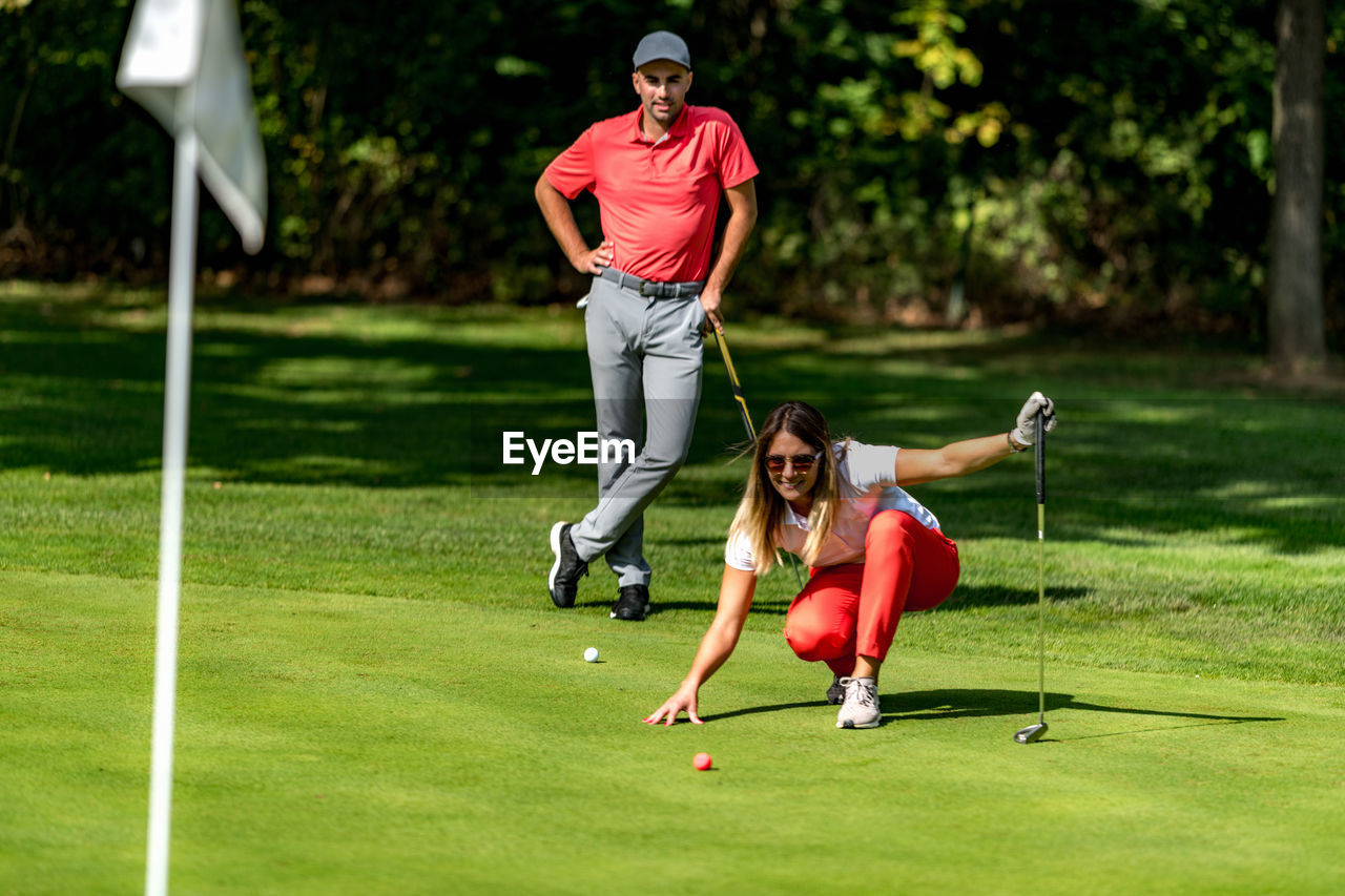 Couple playing golf, young woman reading green, getting ready to putt