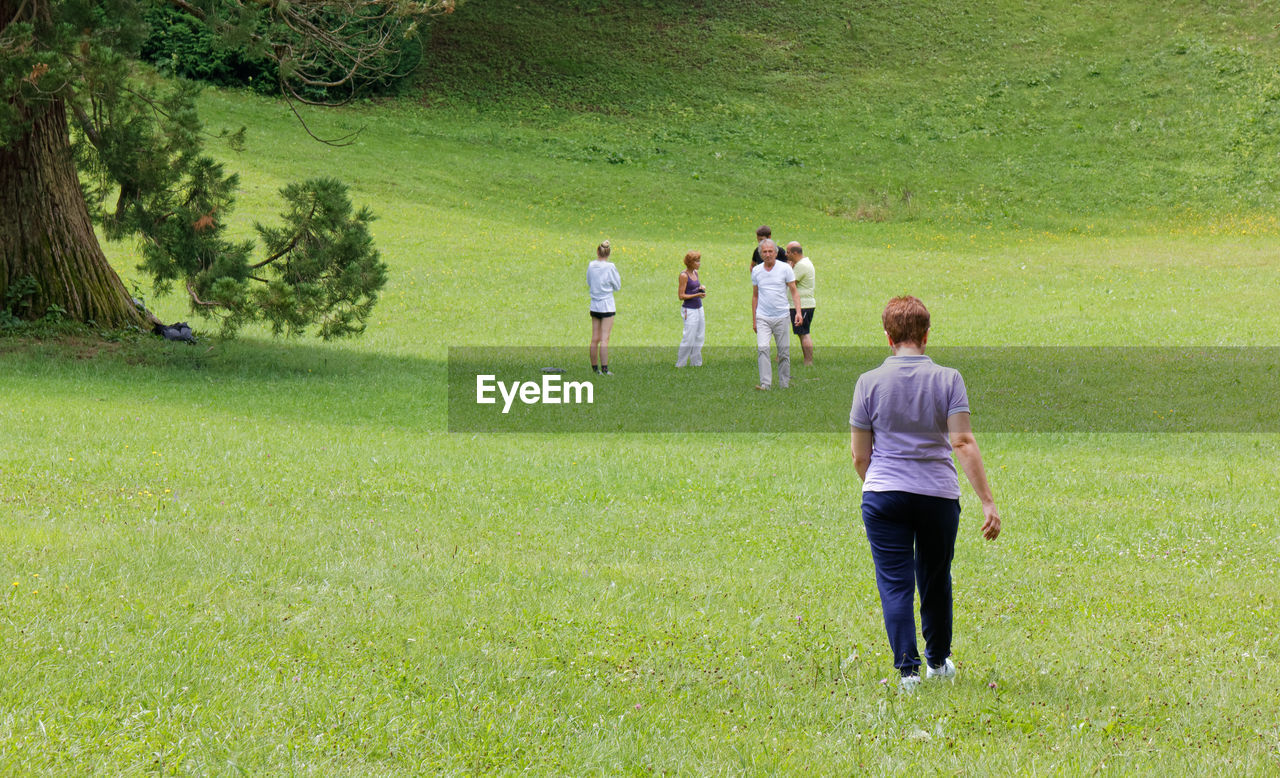 REAR VIEW OF PEOPLE WALKING ON GREEN LANDSCAPE