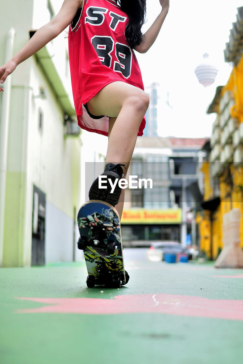 Low section of woman in city playing skateboard