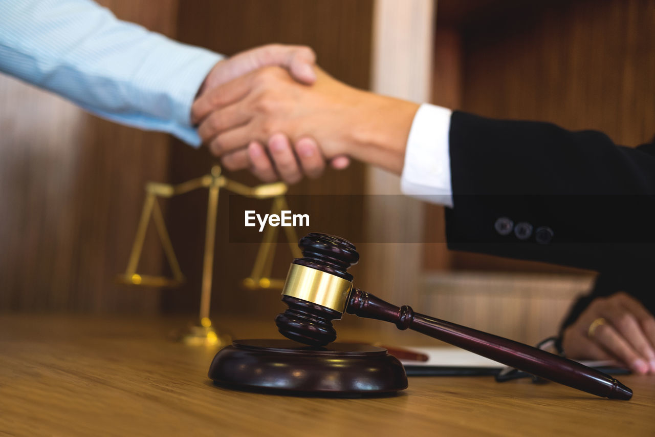 Cropped hands of lawyer giving handshake to client at desk in office