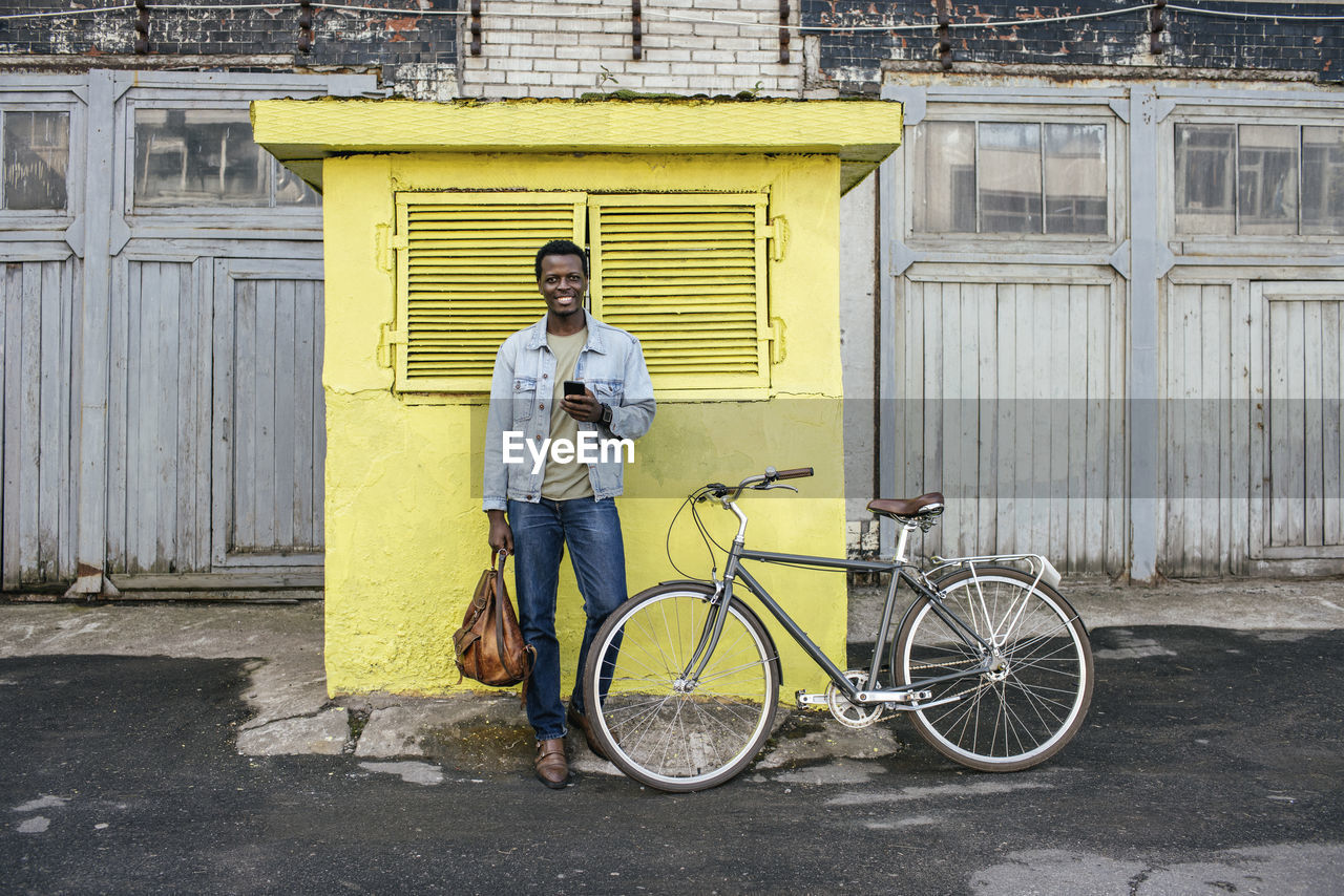 Young man with smartphone, waiting in front of yellow junction box