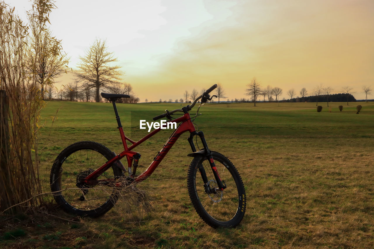 bicycle, transportation, plant, sky, nature, grass, field, mode of transportation, vehicle, land vehicle, land, sports equipment, tree, landscape, environment, no people, sunset, mountain bike, tranquility, soil, cycle sport, beauty in nature, scenics - nature, rural area, tranquil scene, day, outdoors, non-urban scene, cloud, sunlight, rural scene, travel, wheel, parking
