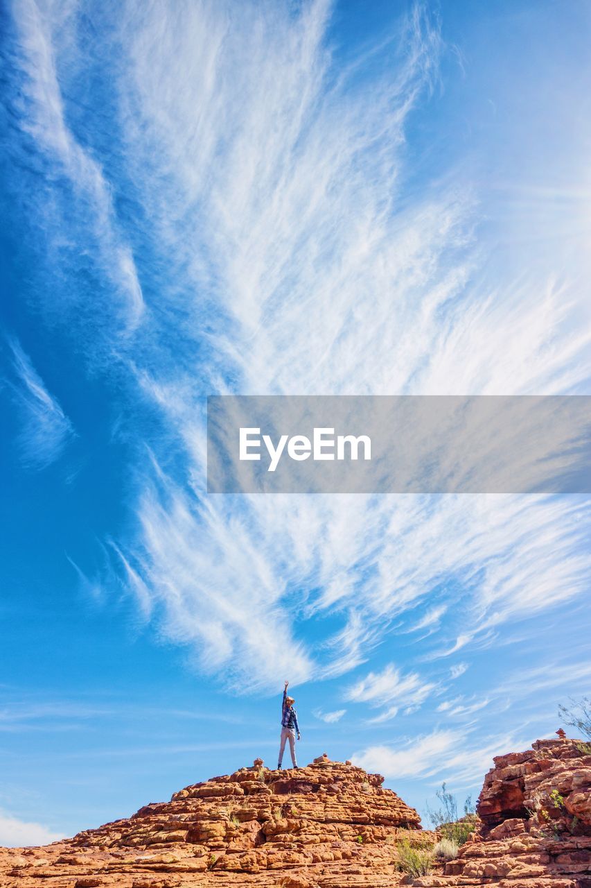 Low angle view of man standing on rock against sky