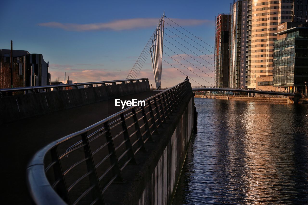 BRIDGE OVER RIVER BY BUILDINGS IN CITY AGAINST SKY