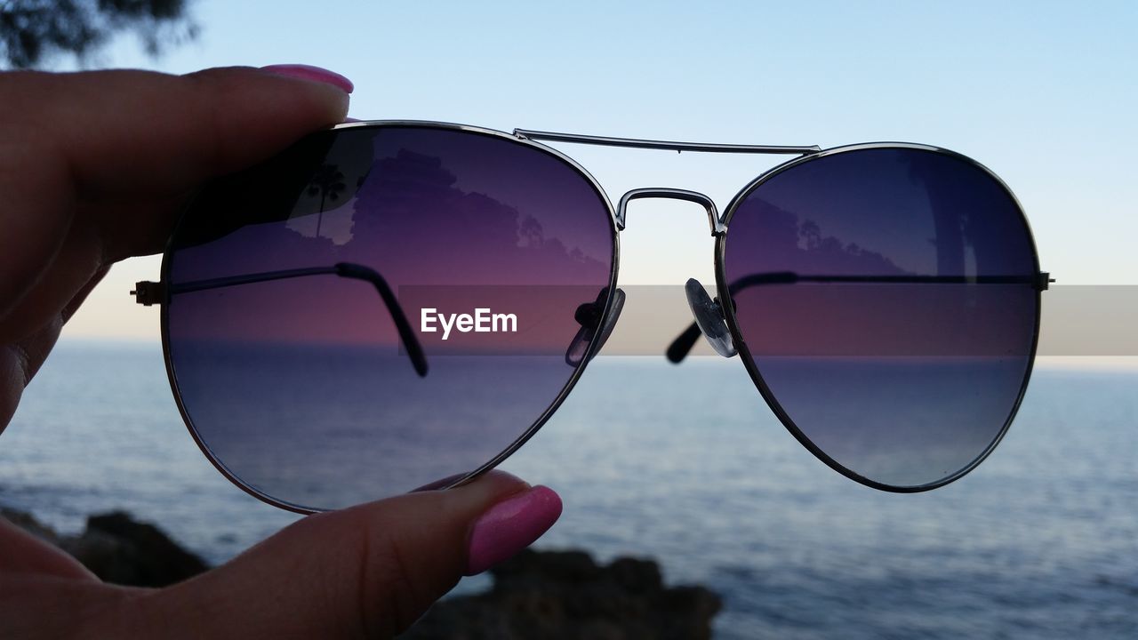 Cropped hand of woman holding sunglasses against sea