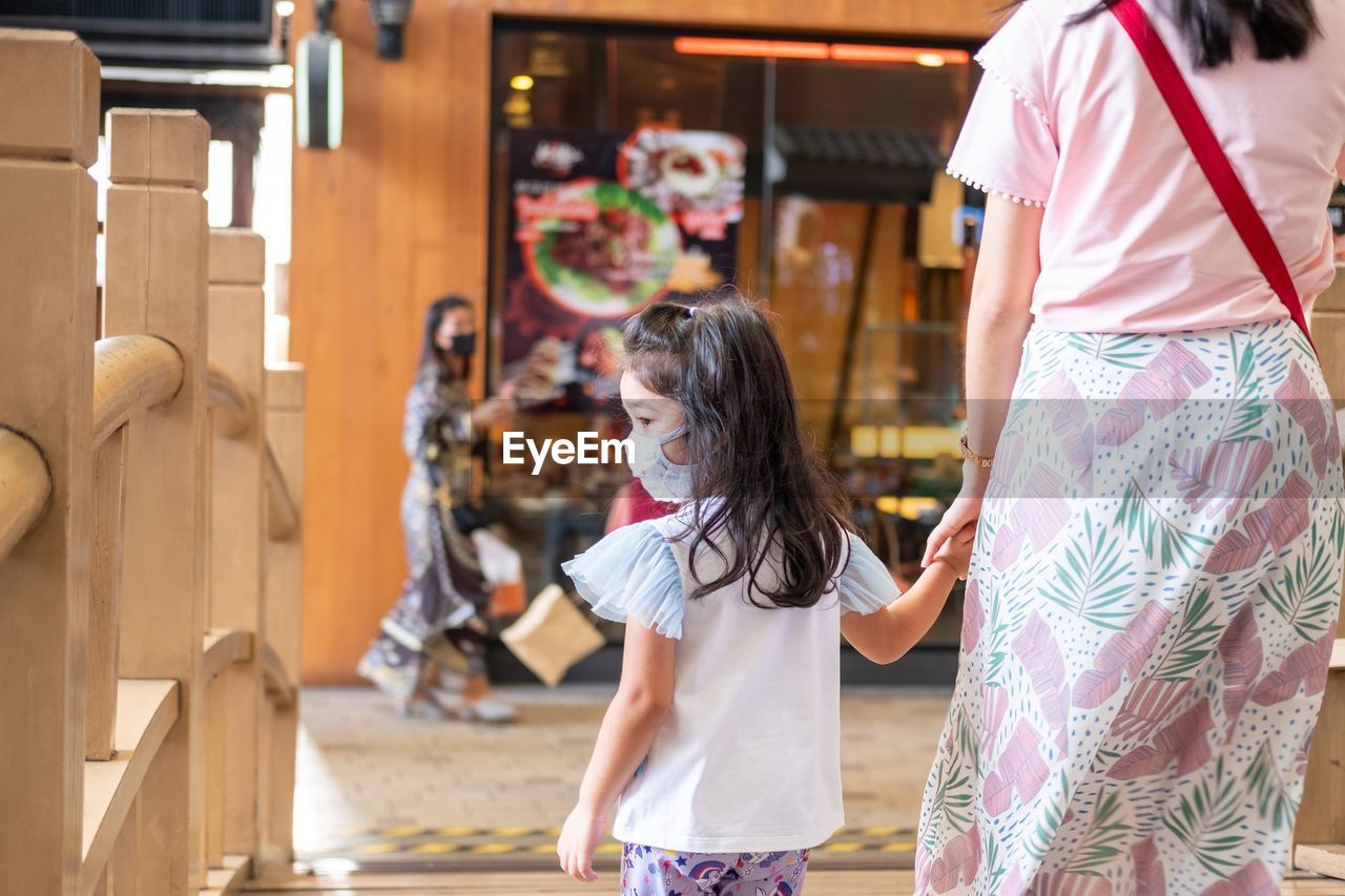 Rear view of daughter wearing mask walking with mother