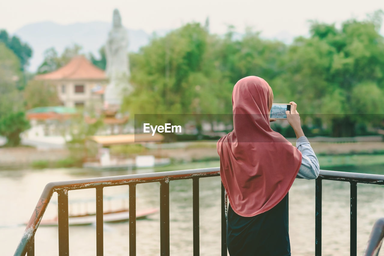 REAR VIEW OF PERSON PHOTOGRAPHING ON RAILING