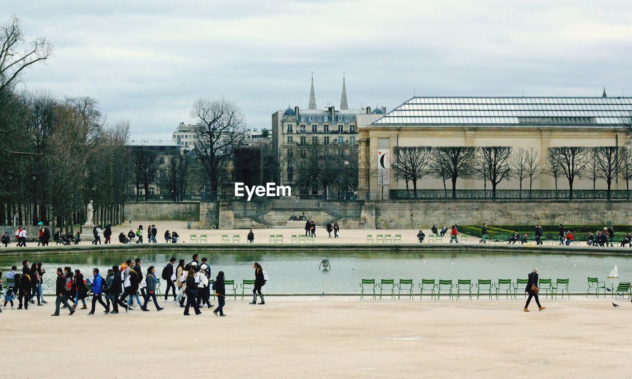 People walking by lake against buildings in city