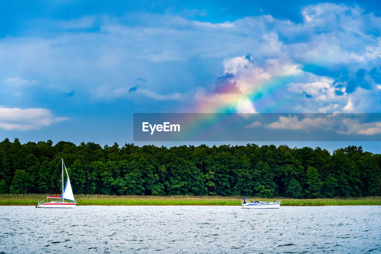 Yacht with white sail on a lake against gloomy rainy blue sky and the rainbow. summer sailing