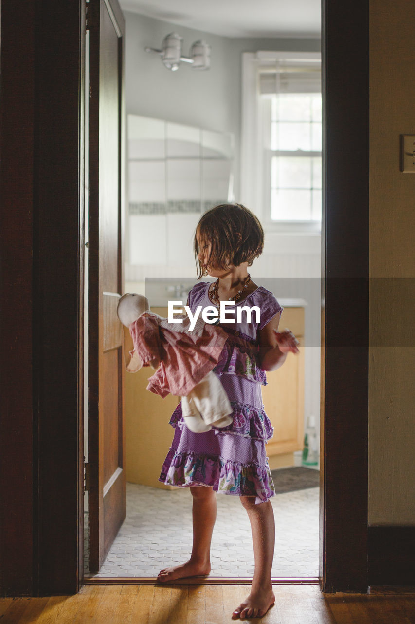 A barefoot child stands alone in doorway holding a stuffed animal barefoot