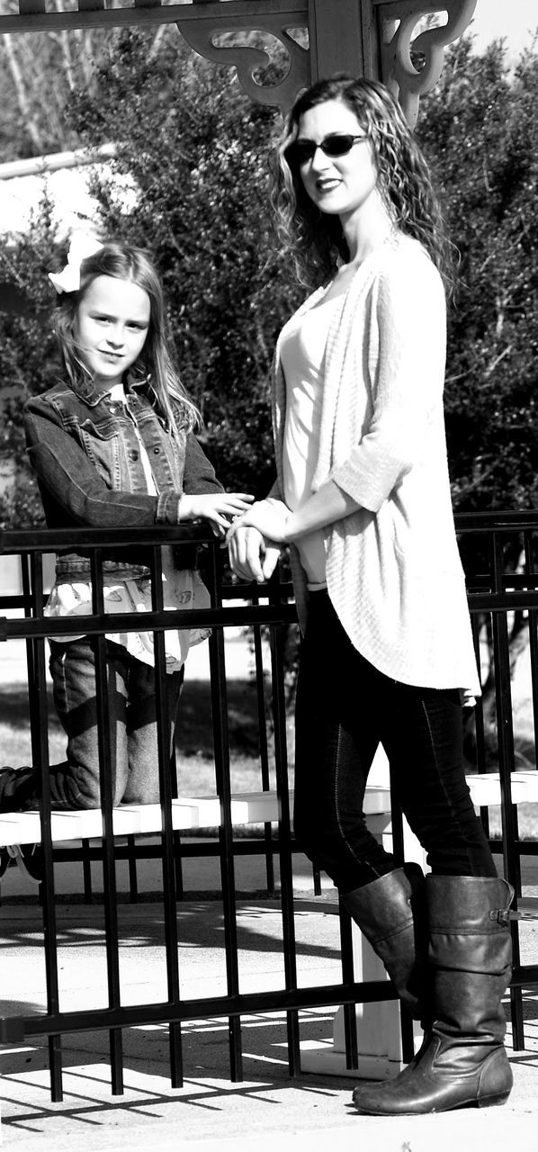 Portrait of mother and daughter standing at railing in park