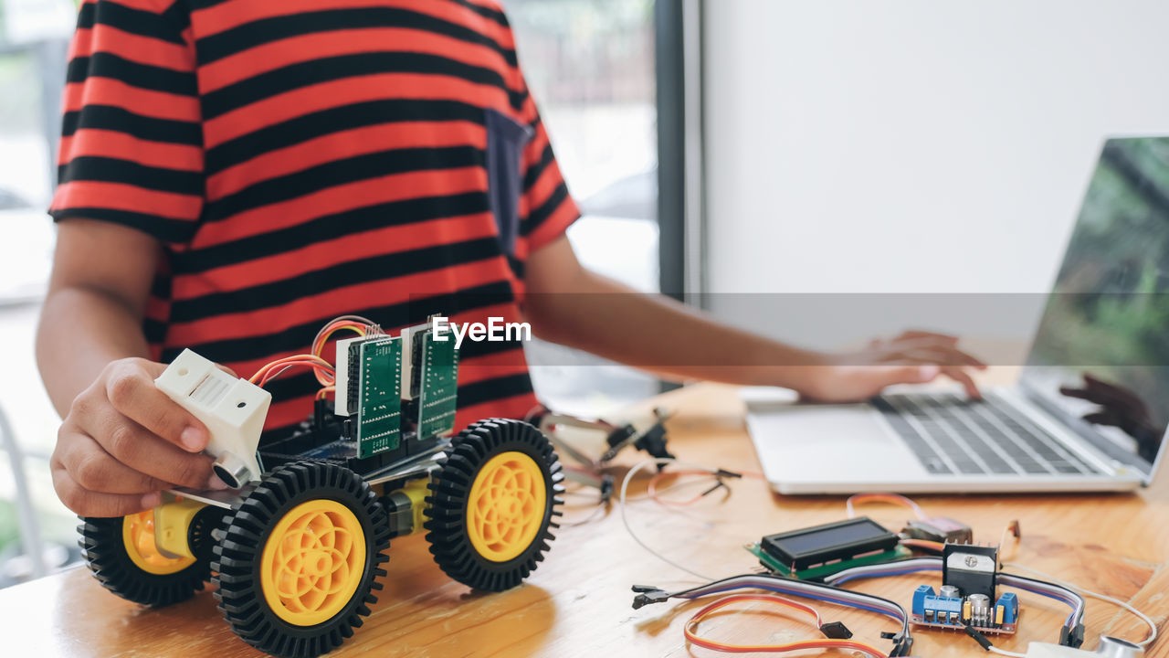 Midsection of boy using laptop while repairing toy on table