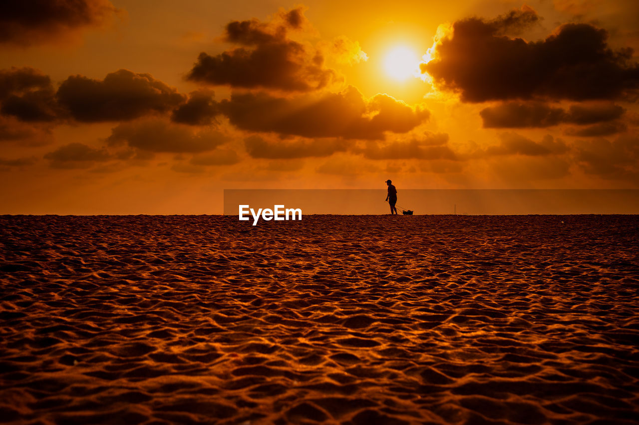 SILHOUETTE MAN ON BEACH AGAINST ORANGE SKY