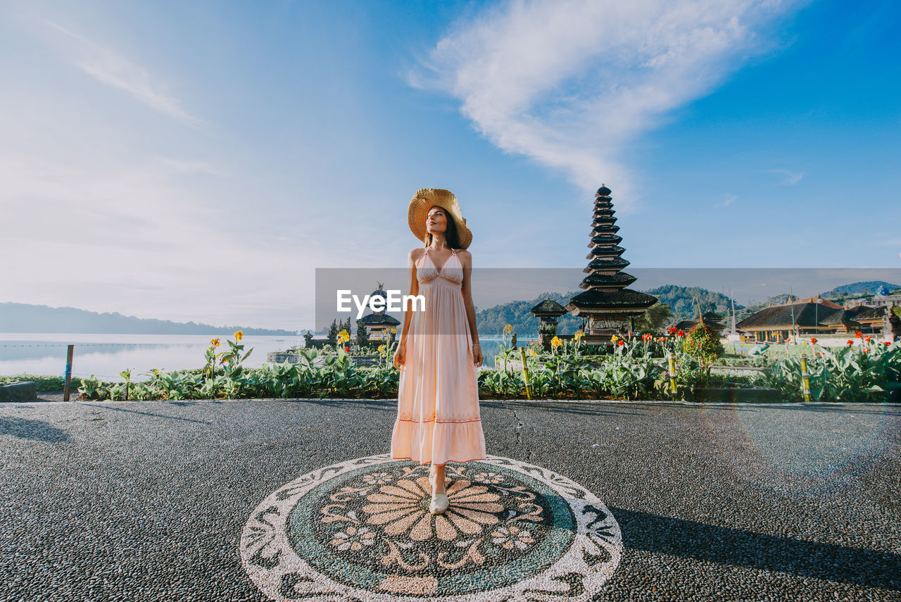 Woman standing at pura ulu danau temple against sky during sunrise