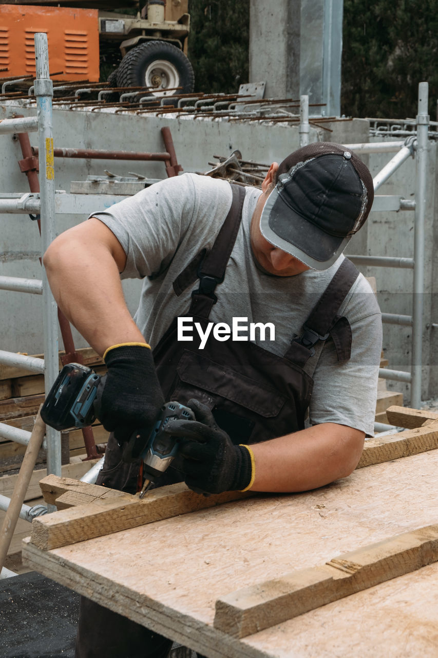 Builder with drill. man carpenter twists a screw into wooden plank with an electric screwdriver