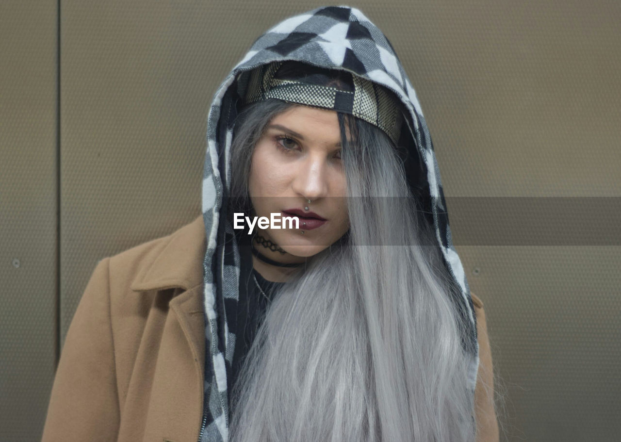 Portrait of woman with dyed hair wearing hooded shirt and jacket against wall