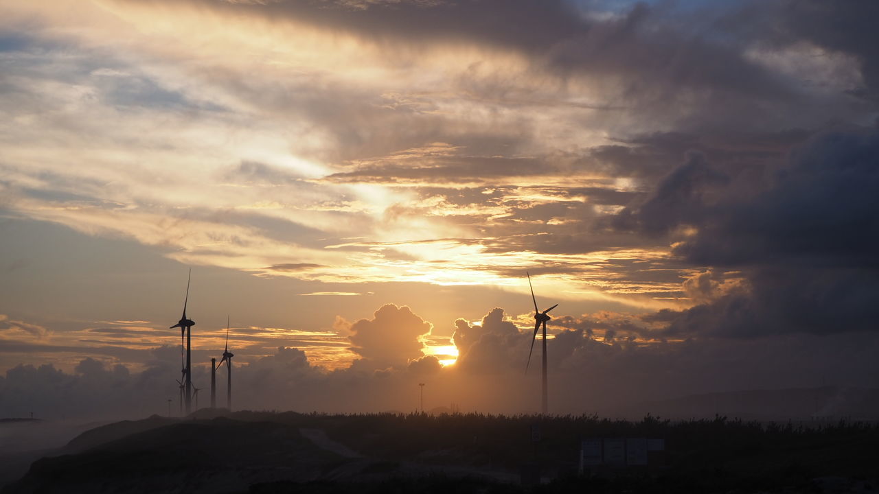 Silhouette electricity pylons against dramatic sky during sunset