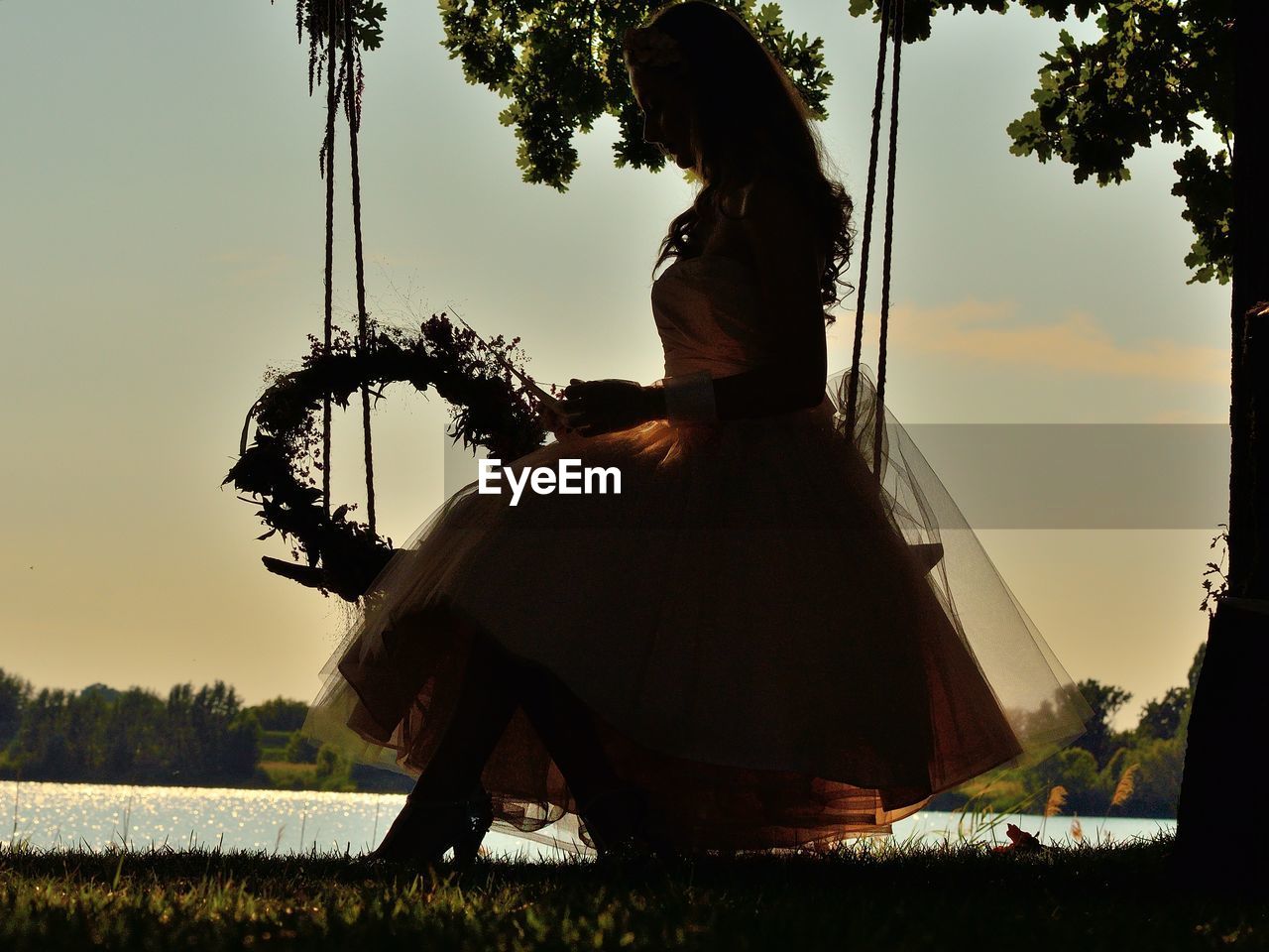 Woman sitting by lake on swing