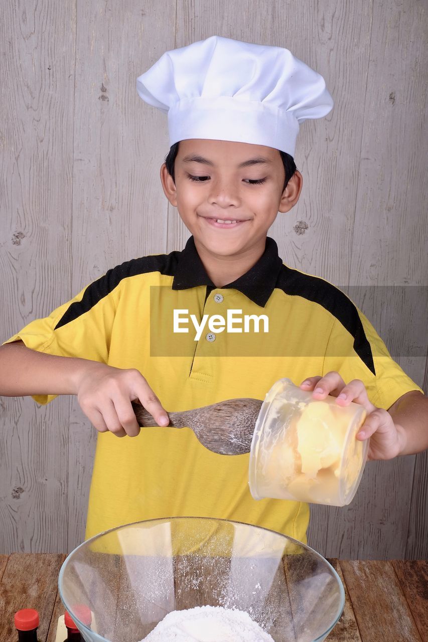 Boy wearing chef hat preparing food in kitchen at home