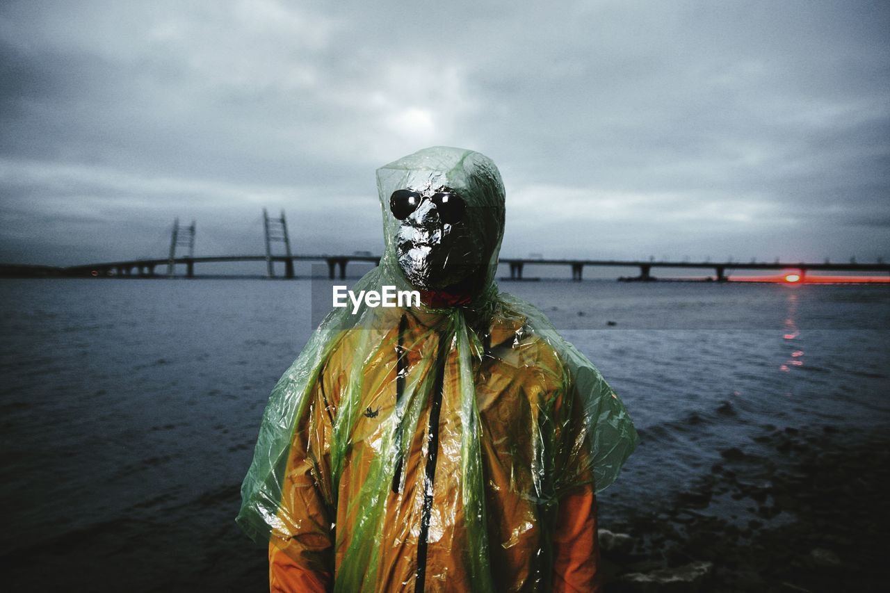 Man wearing mask while standing against sea during sunset