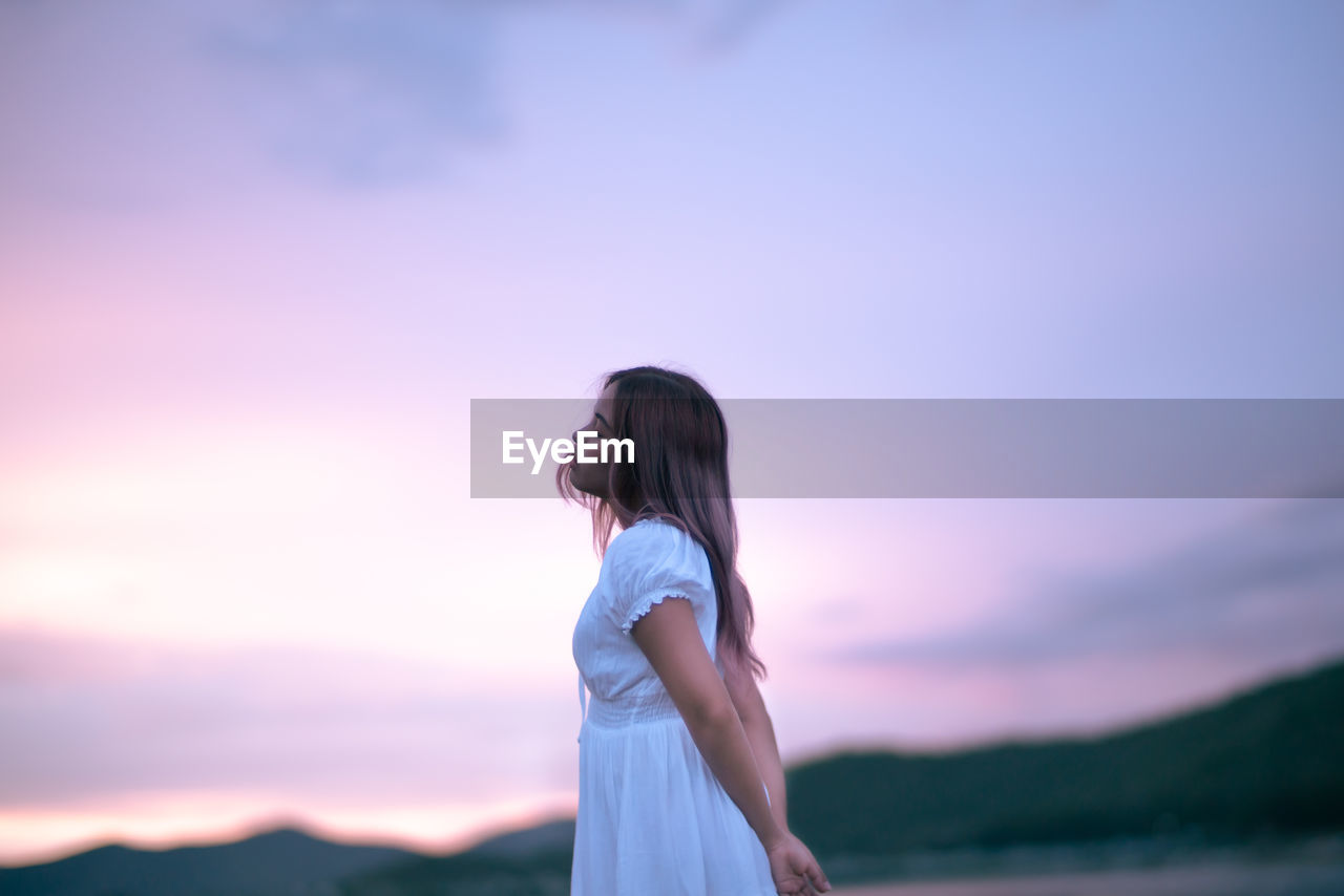 Side view of woman standing against sky during sunset