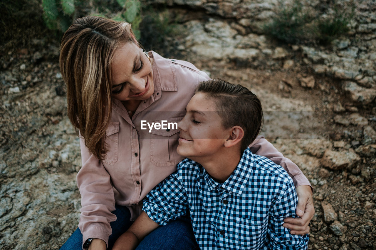 Mother hugging non binary child while sitting on rocks