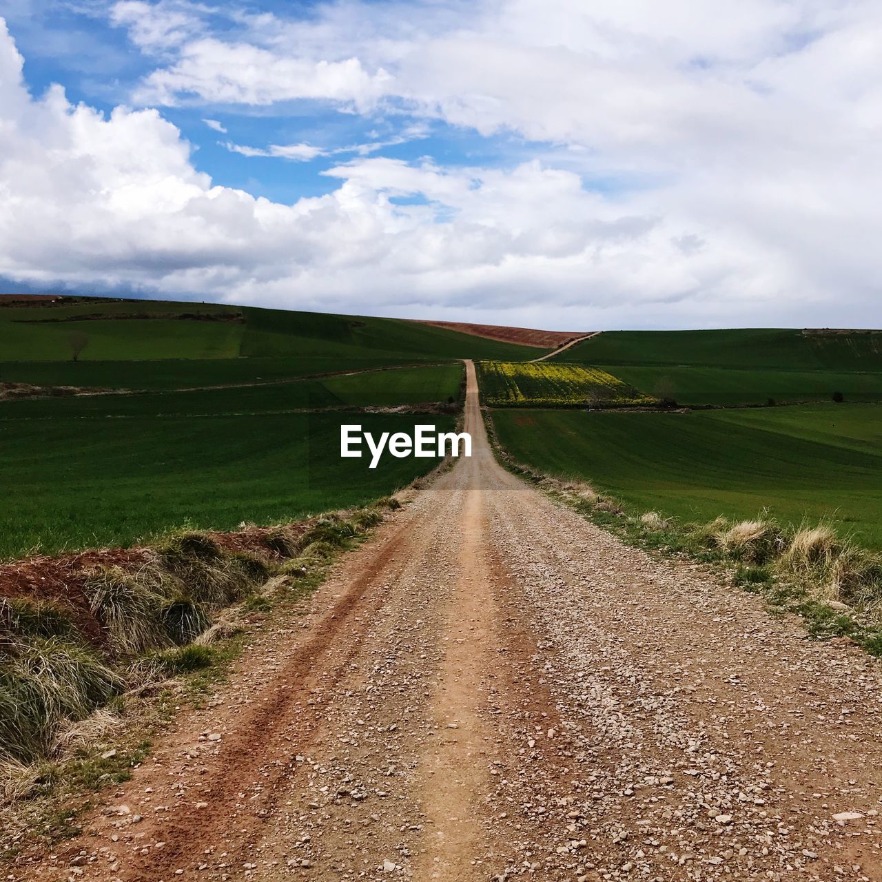 Dirt road amidst field against sky