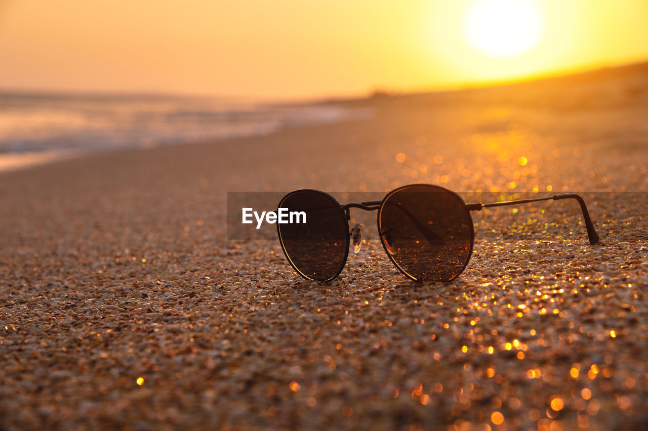 morning, sunlight, land, beach, sky, reflection, nature, yellow, sea, water, glasses, close-up, macro photography, horizon, sunglasses, sunrise, sand, sun, summer, no people, tranquility, fashion, outdoors, selective focus, beauty in nature, scenics - nature, orange color, tranquil scene, travel, holiday, vacation
