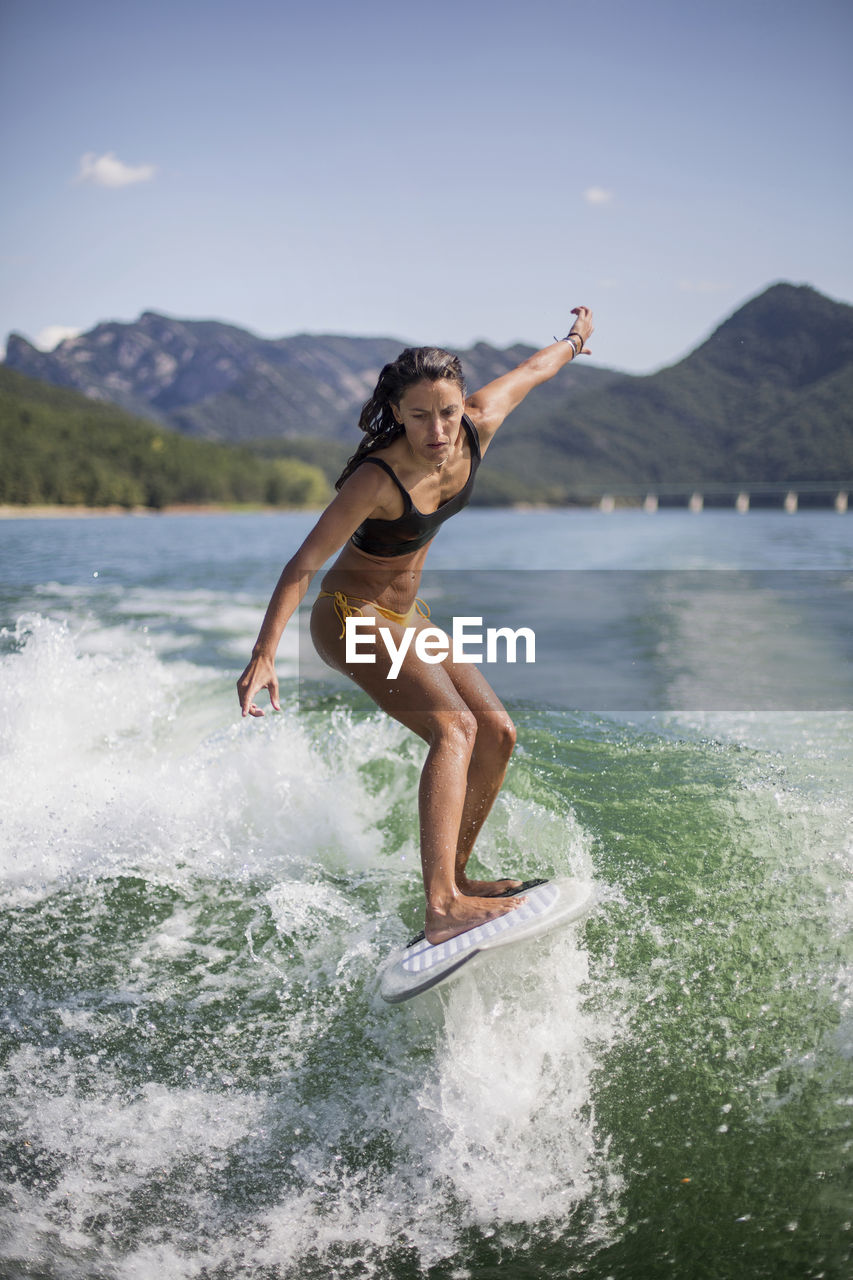 Woman surfing in lake against mountain range