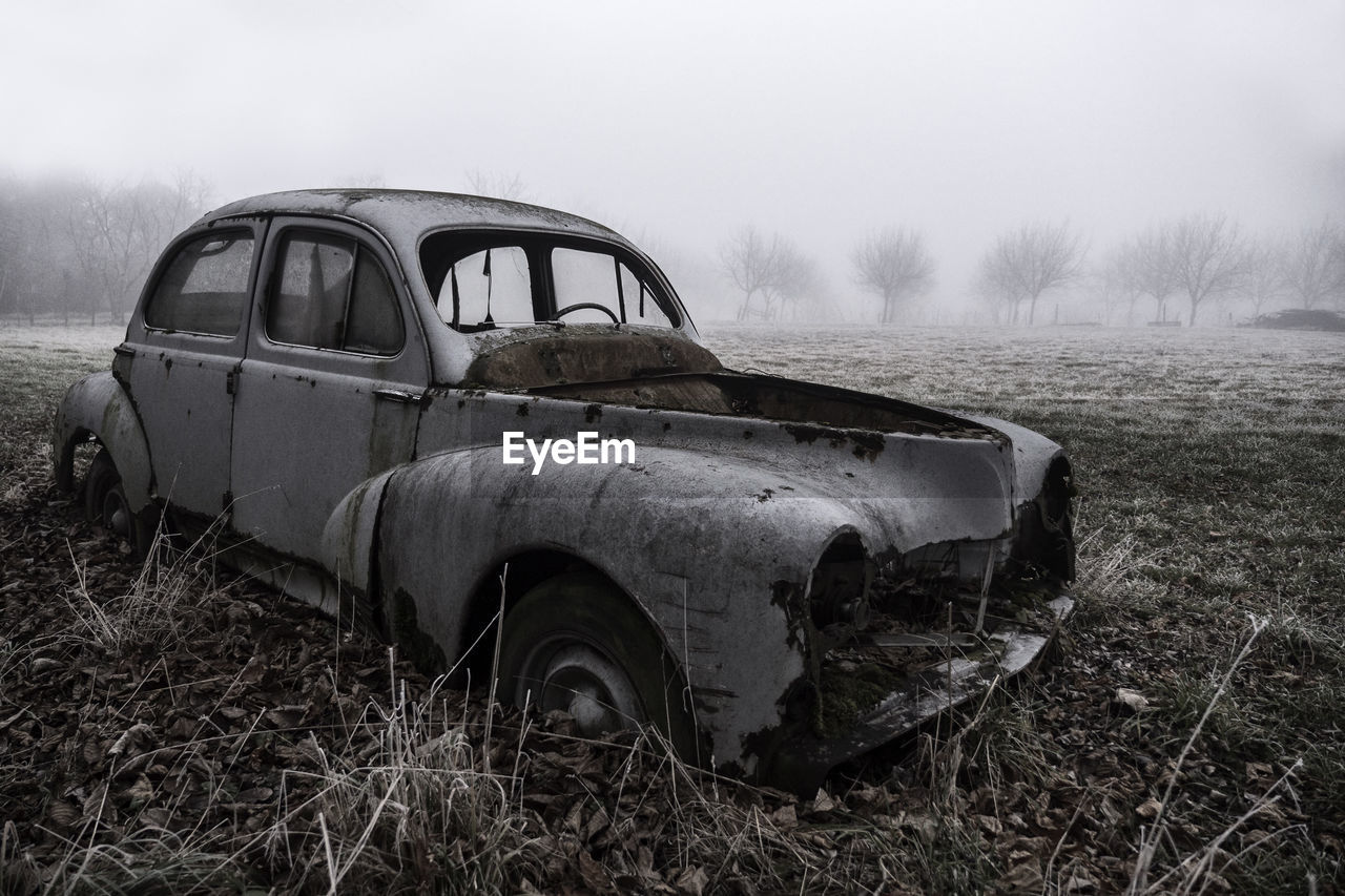 Abandoned car on field against sky