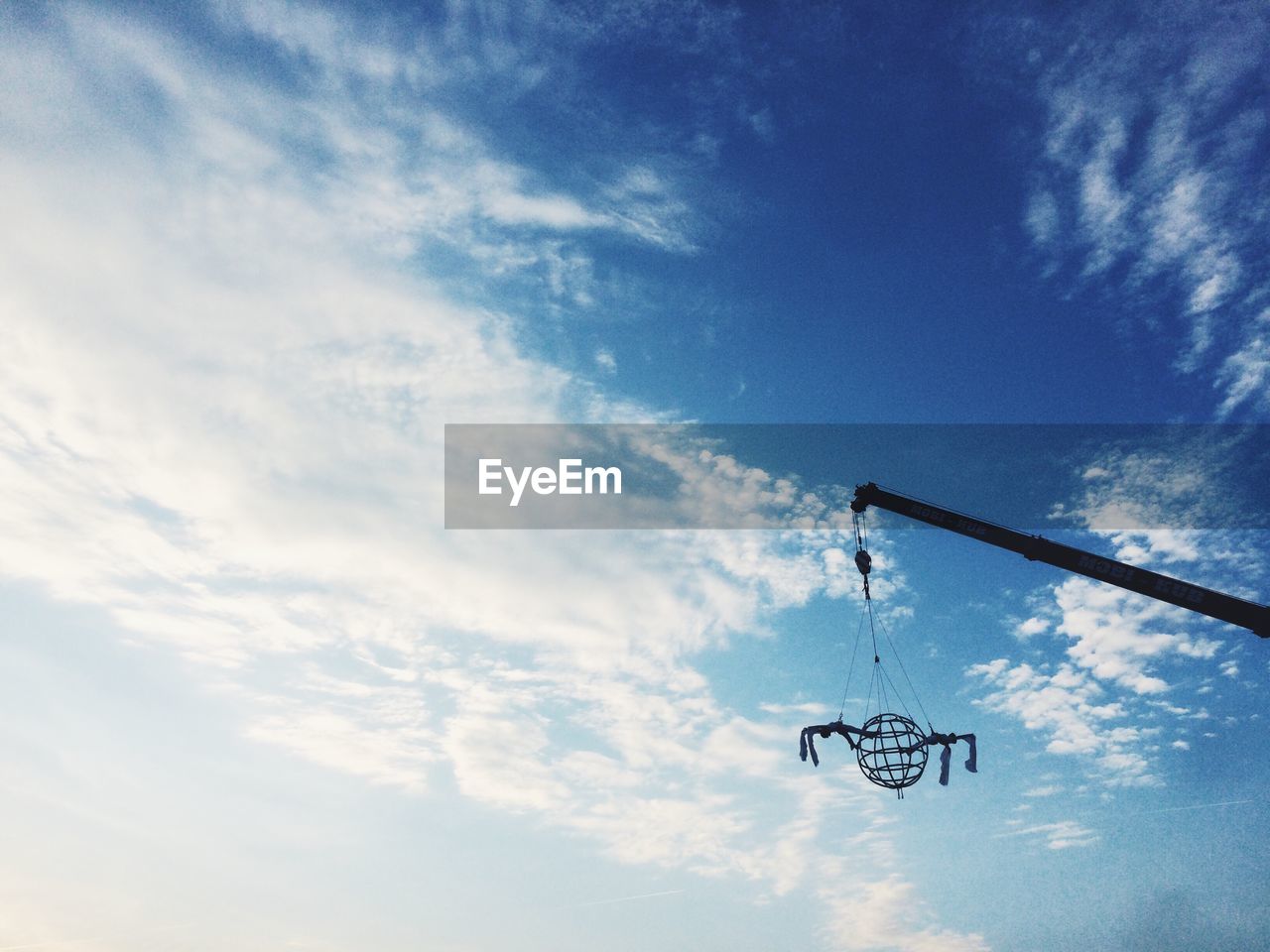 Low angle view of metal hanging on crane against sky