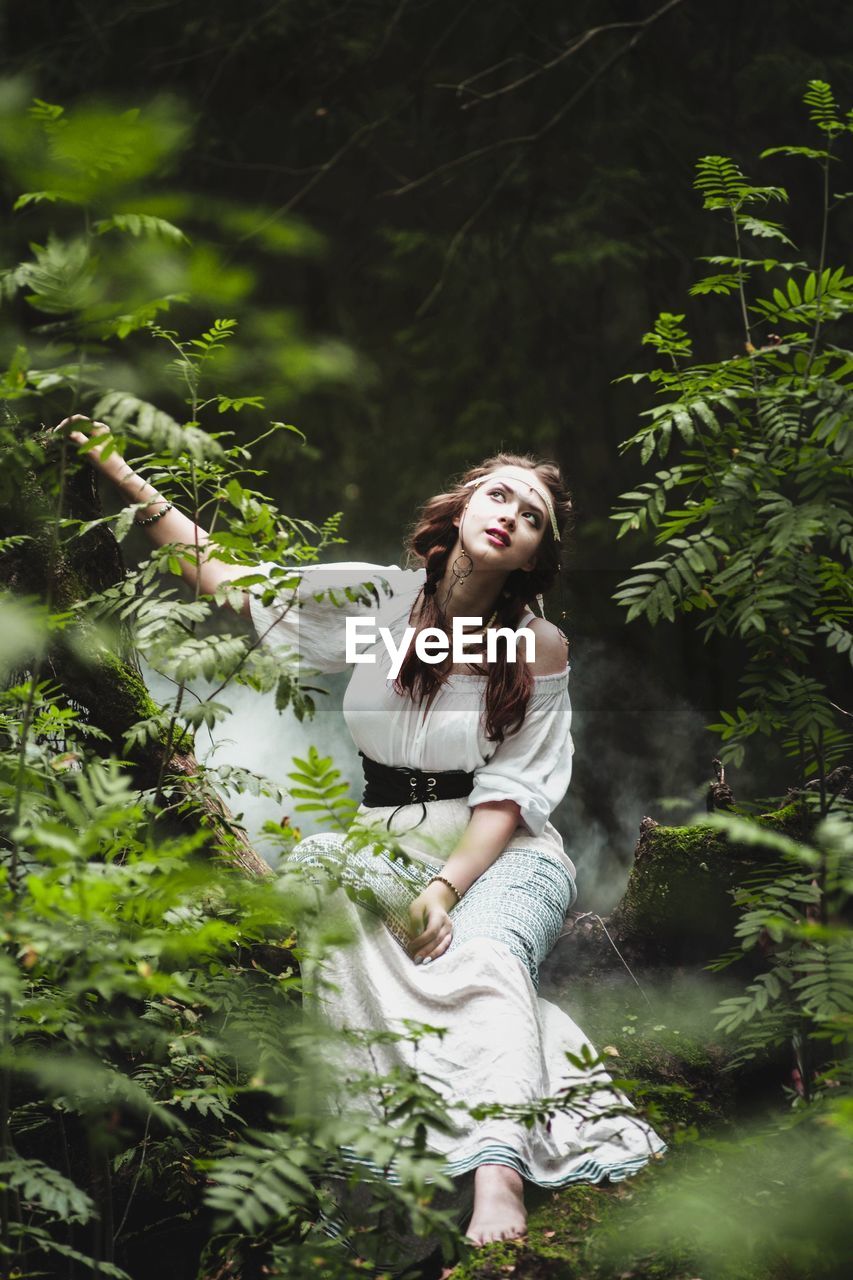 YOUNG WOMAN STANDING AGAINST TREES IN FOREST