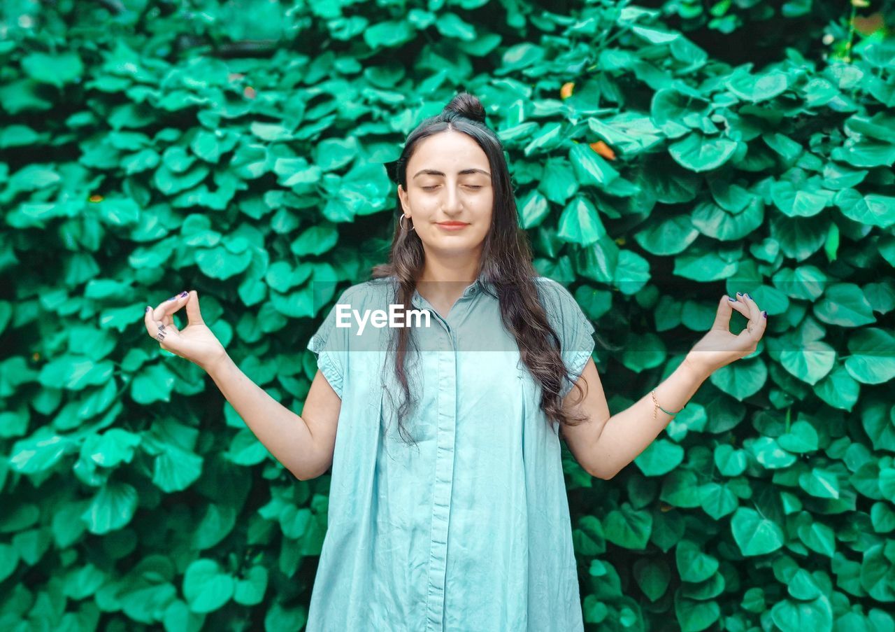 Woman meditating while standing against plants