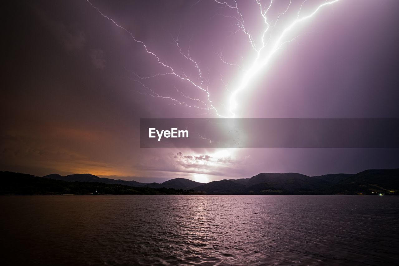 Scenic view of lightning over lake against dramatic sky