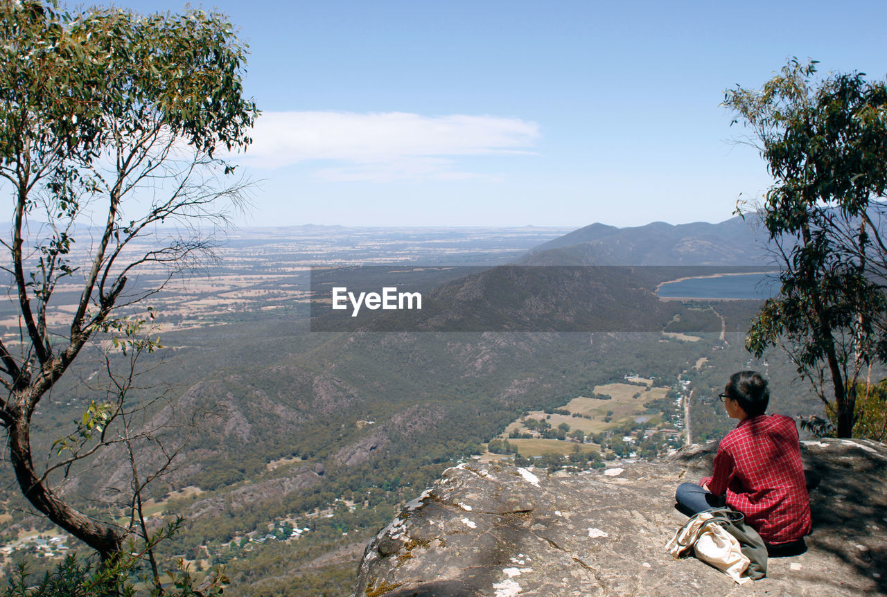 REAR VIEW OF MAN SITTING ON MOUNTAIN