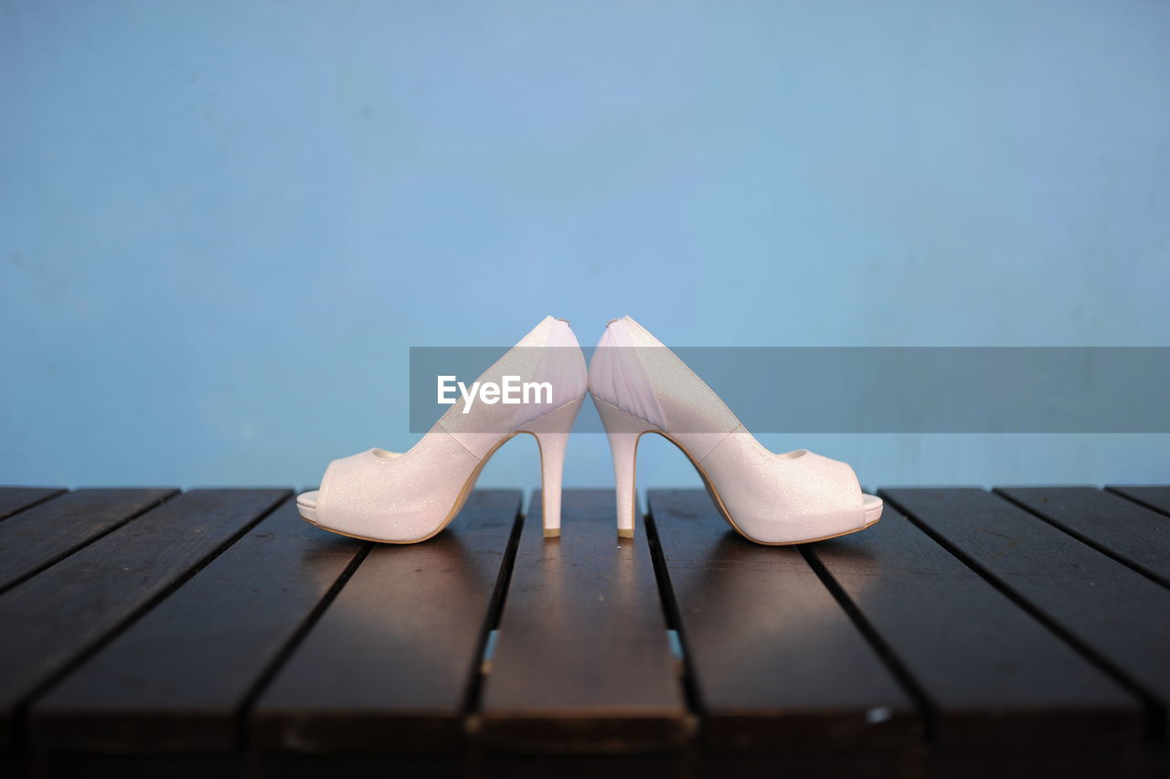 Close-up of high heels on wooden table against blue background