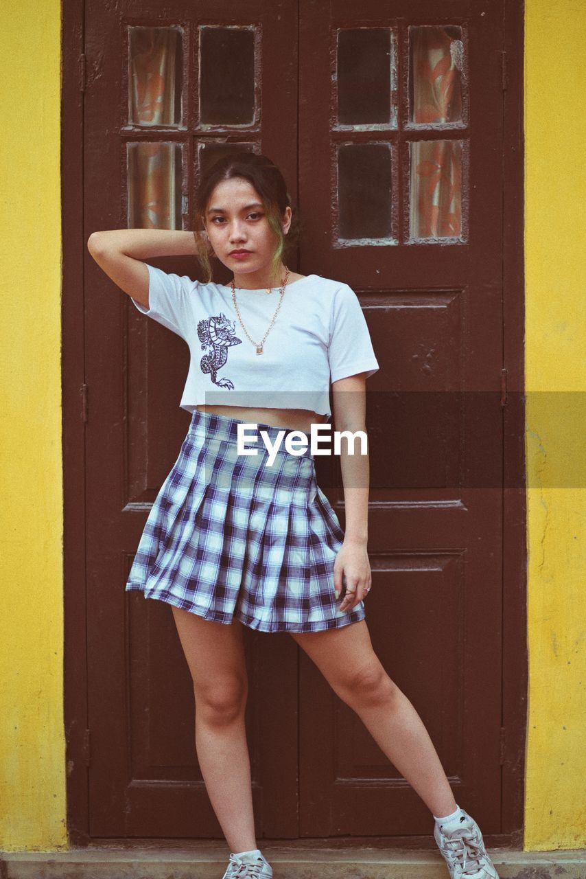 Portrait of teenage girl standing against yellow door