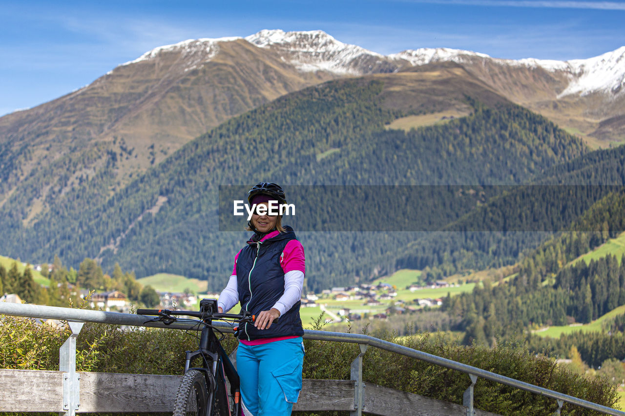 Portrait of woman standing with bicycle by railing against mountains