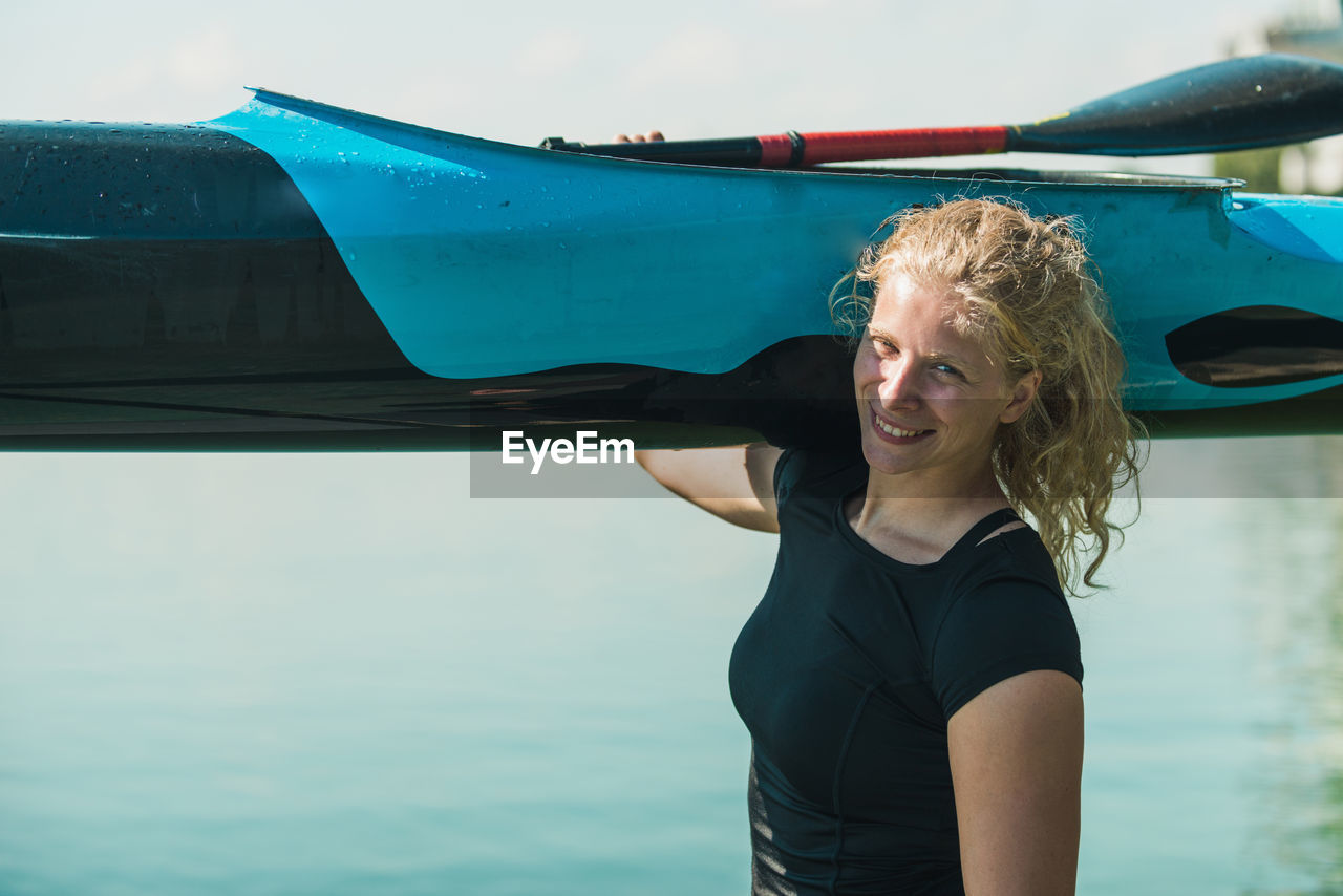 Portrait of smiling young woman carrying kayak