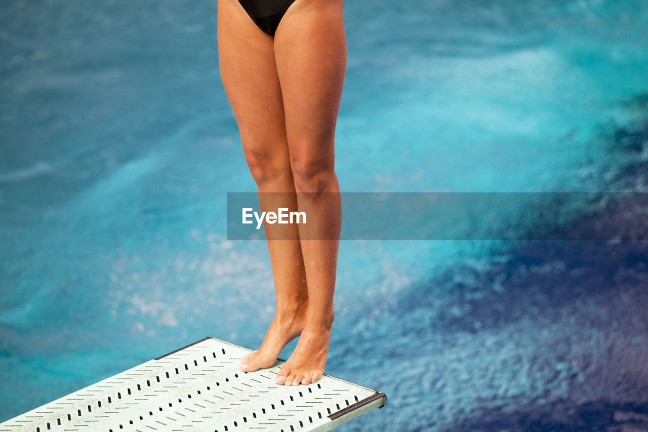 LOW SECTION OF WOMAN STANDING AT SWIMMING POOL