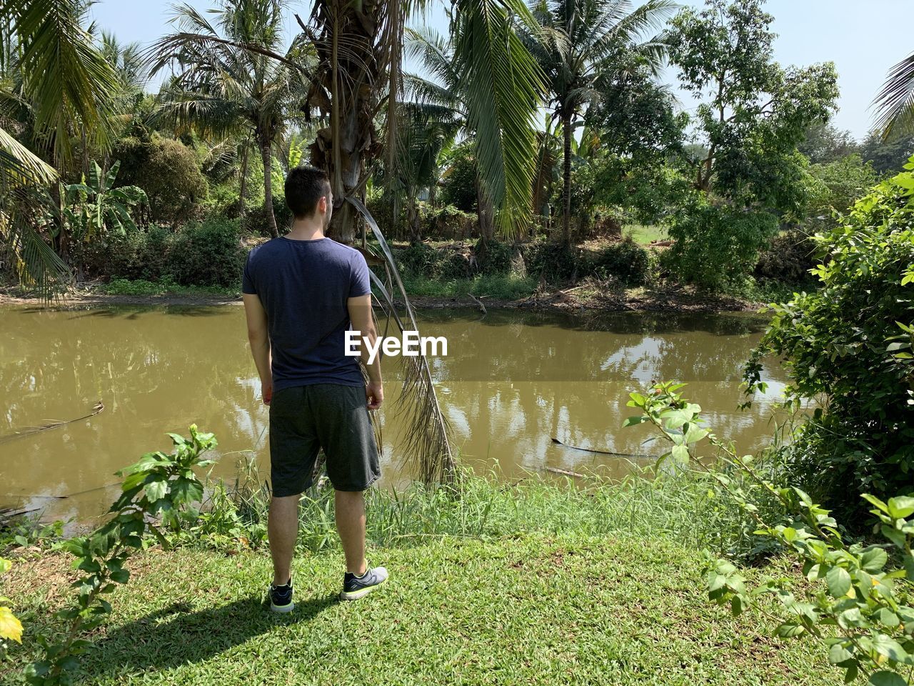 REAR VIEW OF MAN STANDING AGAINST LAKE