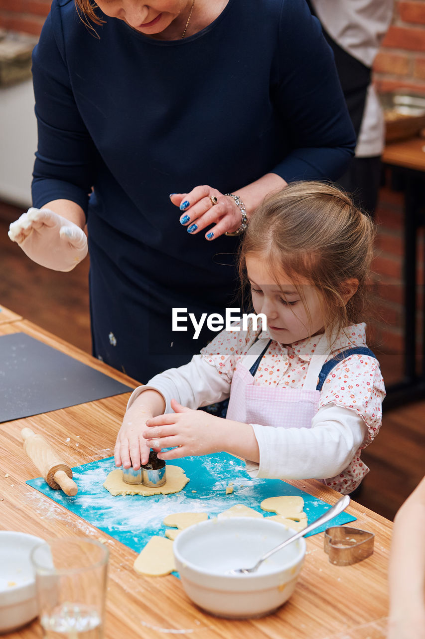 Midsection of woman assisting girl preparing cookie