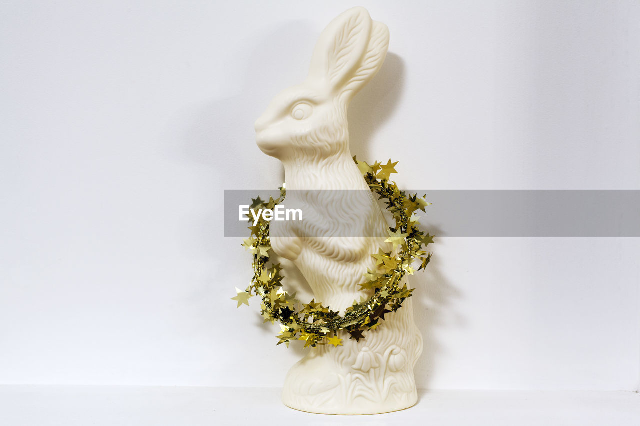 Close-up of figurine with wreath against white background