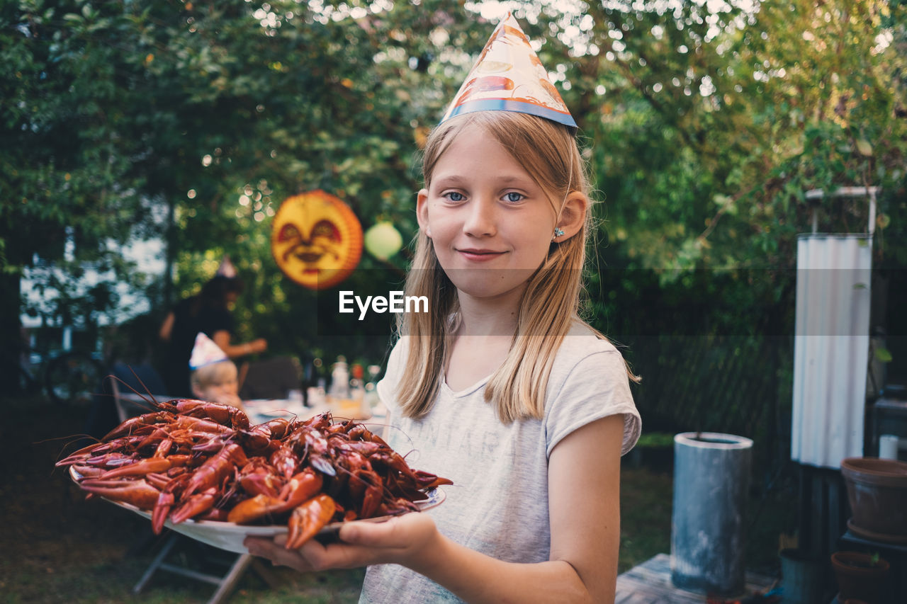 Portrait of girl holding plate with cooked crayfish at garden dinner party